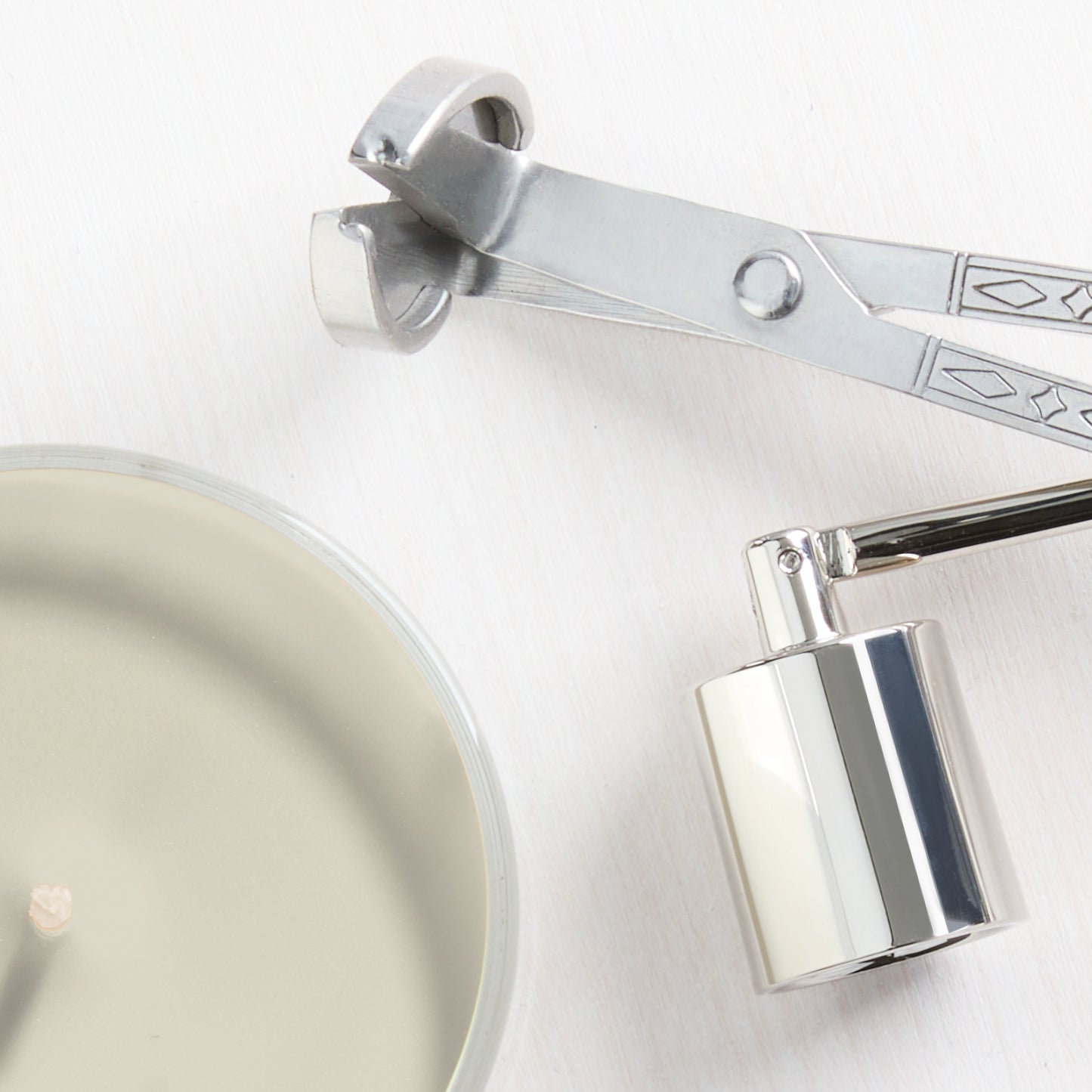 Silver candle wick trimmer and snuffer beside a round soy wax candle for home fragrance and decor.